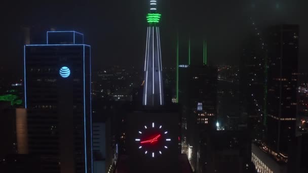 Widok z bliska neonowego podświetlanego kolca i zegara na szczycie Mercantile National Bank Building. Nocny widok drona z powietrza przechyla się w dół. Dallas, Teksas, USA — Wideo stockowe