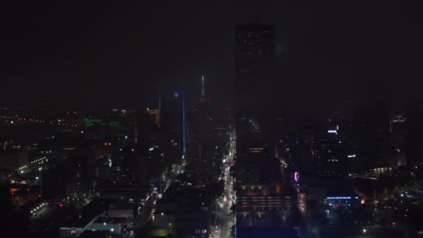 Drohne fliegt über beleuchtete, gerade Straße zwischen hohen Gebäuden rund um das Mercantile National Bank Building mit Turm und großer Neonuhr. Nachtaufnahme der Innenstadt. Dallas, Texas, USA — Stockvideo