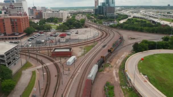 Luftaufnahme eines Güterzuges auf den Gleisen. Gütertransport auf einem Eisenbahnkorridor, der sich zwischen Autobahn und Innenstadt windet. Drohne verfolgt Schienenfahrzeuge. Dallas, Texas, USA — Stockvideo