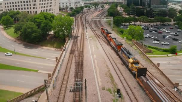 Tres potentes motores diesel que conducen el tren de carga alrededor de rascacielos de fachada de vidrio moderno. Vista aérea del avión no tripulado del tren que llega lentamente a la estación. Dallas, Texas, EE.UU. — Vídeos de Stock