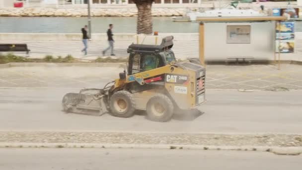 Bobcat с подметальным устройством очистки улицы перед укладкой новой поверхности асфальта. Местный ремонт дорог возле пристани. Улица Лагоса, Португалия — стоковое видео