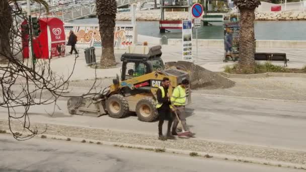 Wheeled front loader cleaning the street before repairing surface. Two workers walking around. Street in Lagos, Portugal — Stock Video