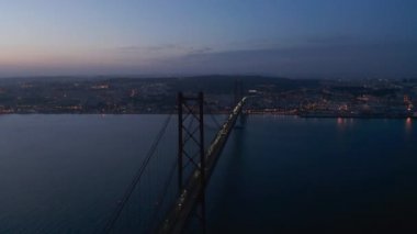 Ponte 25 de Abril kırmızı köprüsünün hava yörüngesinde araba trafiği ve Lizbon şehir merkezi açıklarında ışıklar.