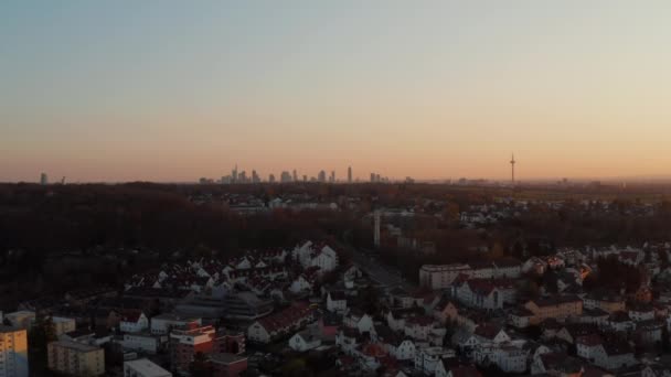 Distante Frankfurt am Main skyline contra o céu crepúsculo. Filmagem de drones revelando casas e ruas em uma pequena cidade termal. Bad Vilbel, Alemanha. — Vídeo de Stock