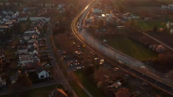 Letecký pohled na dvojkolejnou železniční trať projíždějící okrajem městečka. Nakloněné záběry odhalují zapadající slunce. Příjemná večerní atmosféra. Bad Vilbel, Německo. — Stock video