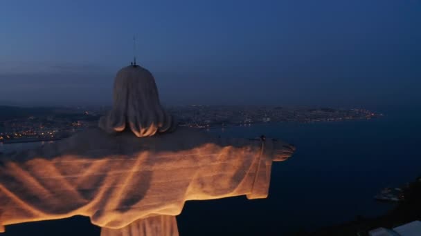 Закрыть воздушный ночной снимок белого монумента Сантуарио де Кристи на холме с центром города Лисбон с огнями на заднем плане — стоковое видео