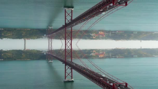 Jam sibuk di jembatan jalan raya. Berbagai mobil mengemudi di jembatan gantung merah besar di atas sungai yang luas. Komputer menambahkan efek cermin horisontal. Lisbon, Portugal. — Stok Video