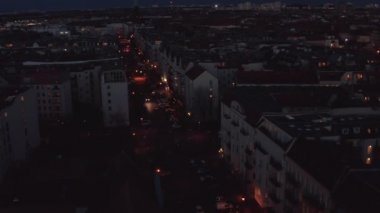 İkametgah semtindeki yolda giden araçları takip ediyoruz. Gün batımından sonra park etmiş arabalarla geniş caddenin havadan görüntüsü. Berlin, Almanya.