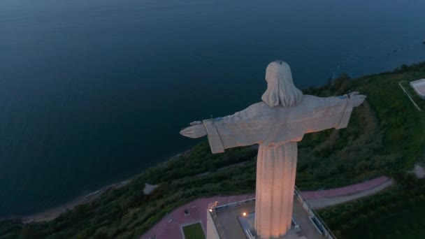 Orbita aérea de primer plano de gran monumento blanco del Santuario de Cristo Rei y puente rojo Ponte 25 de Abril frente a la costa de Lisboa, Portugal en 2021 — Vídeo de stock