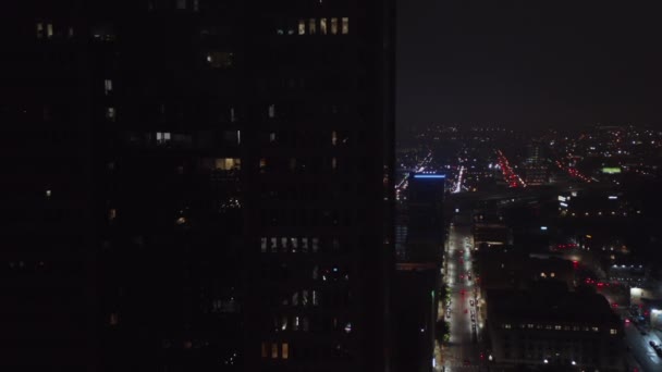 Avances aéreos vuelan hacia un edificio alto. Calles iluminadas por la noche. Bajo tráfico conduciendo por carretera en segundo plano. Dallas, Texas, EE.UU.. — Vídeos de Stock