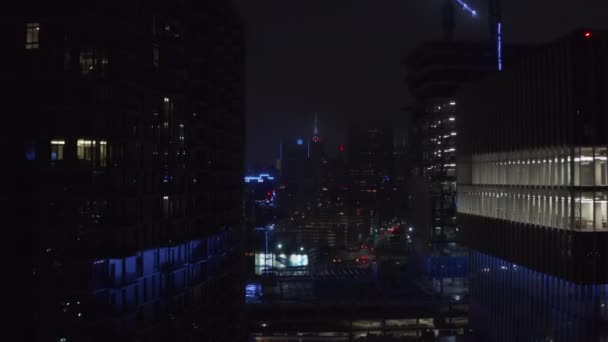 Vpřed létají mezi vysokými komerčními budovami směrem k budově Mercantile National Bank s věží a velkými neonovými hodinami. Noční letecký výhled do centra. Dallas, Texas, USA. — Stock video