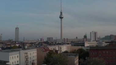 İleride, hava kararınca Fernsehturm 'un etrafındaki kentsel mahalleler ortaya çıkacak. Gözcü platformu ve restoranı olan uzun televizyon kulesi. Berlin, Almanya.