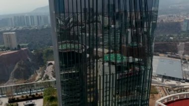 Yüksek açılı modern cam kaplı bina. Paradox Torre gökdeleninde uçan insansız hava aracı kamerası. Çevredeki binaları yansıtan parlak bir cephe. Mexico City, Meksika.
