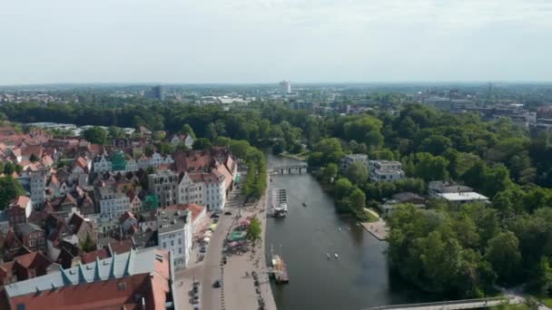 Flygfoto parasoller på terrasser av restauranger vid vattnet. Bred gata längs floden Trave och historiska gamla stan. Luebeck, Schleswig-Holstein, Tyskland — Stockvideo