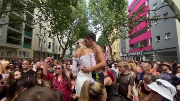 Jovem e mulher de pé no pódio sussurrando no ouvido com uma multidão de pessoas dançando e aplaudindo durante o The Christopher Street Day em Berlim, durante o dia — Vídeo de Stock