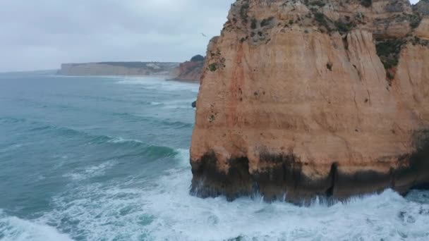 Aerial drone tilt to birds eye overhead top down view reveals strong waves crashing against rocky coastline cliff in Lagos, Portugal — Stock Video