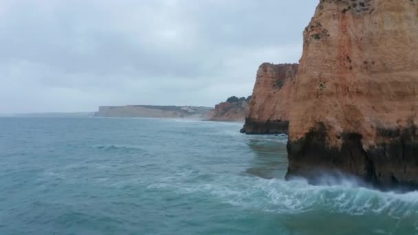 Aerial drone flying low above ocean waves by high orange colored cliffs, Lagos, Algarve, Portugal, dolly in, cloudy day — Vídeos de Stock