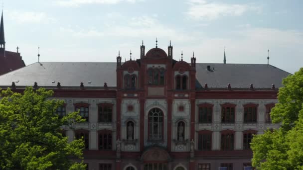 Backwards rising reveal of grown trees on small square in front of historical university building and surrounding streets — Stock videók