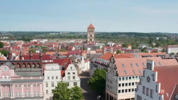 Forwards fly above city hall towards old tower of Nikolaikirche church. Aerial view of various building with tiled roofs — Stockvideo