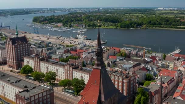 Αεροφωτογραφία της πόλης που βρίσκεται στην όχθη του ποταμού. Κεντρικό φαρδύ δρόμο με τεράστια κτίρια. Πετάξτε πάνω από την εκκλησία Saint Marys κόκκινο κεραμίδι οροφή και τον πύργο — Αρχείο Βίντεο