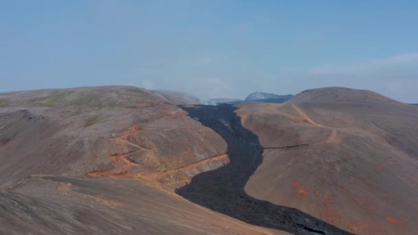 Udara berputar-putar di sekitar sungai lava hitam mengalir antara pegunungan di Fagradalsfjall, Islandia, hari — Stok Video