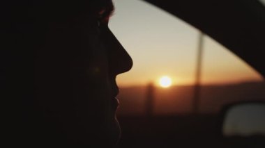Araba kullanırken insanın yandan görünüşü. Romantik gün batımına ve renkli gökyüzüne karşı erkek yüzü silueti