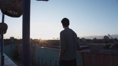 Şehirdeki terasta yürüyen bir adamın görüntüsü. Yetişkin bir erkeğin güneşin doğuşundan ya da batışından keyif alışının arka görüntüsü. Fas, Afrika