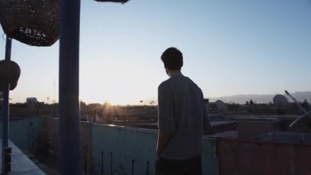Tracking vista dell'uomo che cammina sulla terrazza sul tetto della città. Vista posteriore del maschio adulto medio che si gode l'alba o il tramonto. Marocco, Africa — Video Stock