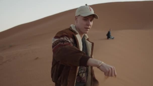 Hombre caucásico adulto jugando con arena fina en el desierto, vertiéndola de la mano y dejándola a la deriva en el viento. Marruecos, África — Vídeos de Stock
