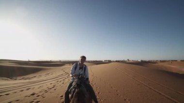 Deve binicisinin izini geriye doğru takip ediyoruz. Çölde evcil hayvanlara binen turistler. Fas, Afrika