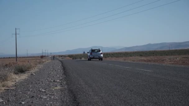 Vista a basso angolo di auto che si allontanano. Linee elettriche che attraversano la strada in un paesaggio asciutto e polveroso in campagna. Marocco, Africa — Video Stock