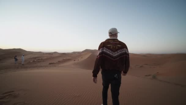 Uomo adulto caucasico godendo mattina nel deserto. Raccogliendo sabbia nelle mani, rilasciandola gradualmente e lasciandola andare alla deriva nel vento. Marocco, Africa — Video Stock