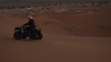 Alacakaranlık vakti çöl kumunda dörtlü sürüşün görüntüleri. Kum tepeciğinin kenarına dikkatle sür. Kuru arazi. Fas, Afrika