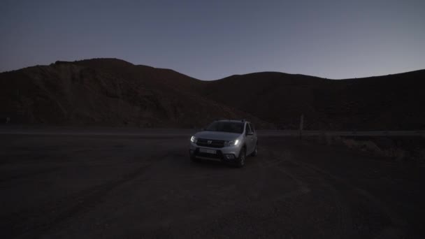 Auto sjíždí ze silnice, zatáčí a zastavuje. Sledování malého stříbrného SUV. Večerní záznam po západu slunce. Maroko, Afrika — Stock video