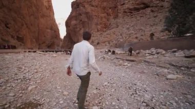 Kayalık arazide yürüyen bir adamın izini sürüyorum. Siyah keçi sürüsünün yanından geçen sıradan giysili bir erkek. Fas, Afrika