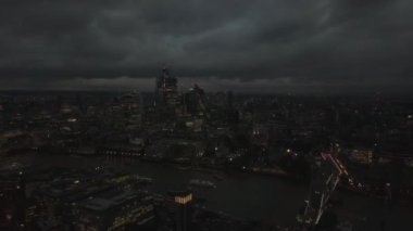 Londra finans bölgesi gökdelenlerinin hava aracı görüntüsü panorama, binaların ve Thames nehrinin üzerinde geriye doğru uçan insansız hava aracı, gece