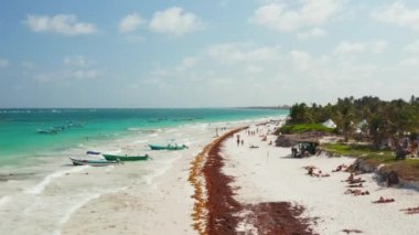 Haftasonu bulutlu bir günde tropikal bir plajda dinlenen ve Meksika 'da Tulum' da yüzmek üzere tekneye binmeye hazırlanan çadırların ve kalabalığın geriye dönük hızlı hareket görüntüsü.