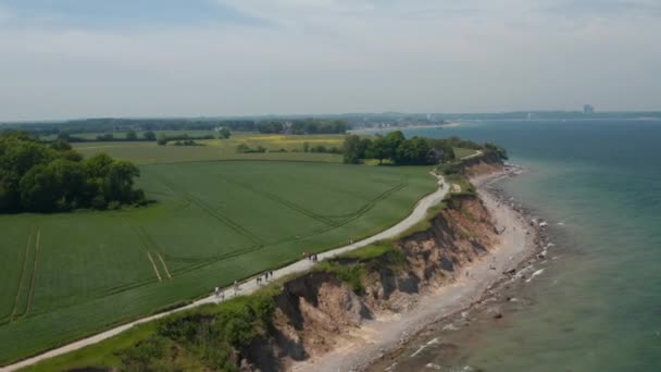 Rustige omgeving in Brodten, Duitsland, luchtfoto drone uitzicht op de kust van het strand met uitzicht op de Oostzee met uitgestrekte groene lente veld, dolly in, dag — Stockvideo