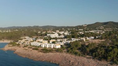 İspanya 'nın İbiza şehrinde açık bir gökyüzü gününde ev ve tatil köyüyle çevrili sessiz ve sakin bir deniz manzarası.