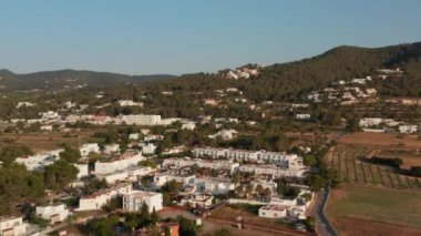 İspanya 'nın güzel şehri İbiza' da akşam saatlerinde yeşil ve dağlarla çevrili, park halindeki arabaları ve caddeleri olan güzel beyaz evlerin hava yavaş çekim görüntüsü.