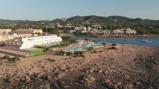 Establecimiento de un tiro de una piscina vacía en el complejo rodeado de carretera rocosa y el océano con barcos aparcados y yate con vistas a la ciudad y la montaña en Ibiza en España — Vídeos de Stock