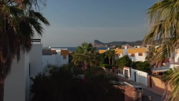 Einrichteraufnahme schöner weißer Villen-Häuser mit Autos, die auf einer leeren Straße vor dem Tor an der Küste der Stille und Ruhe auf Ibiza in Spanien geparkt sind — Stockvideo