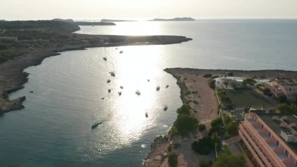 Luchtfoto van boten geparkeerd in een stille en rustige zee met een leeg resort aan de kust met een voetbalveld en groen in Ibiza in Spanje — Stockvideo