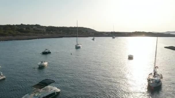 Повітряний вид на човни, припарковані в тихому тихому й тихому морі, оточені горою й зеленню під час заходу сонця в Ібіці (Іспанія). — стокове відео
