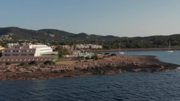 Вид с воздуха на тихую и спокойную океанскую воду, текущую на побережье с курортами и виллами в доме отдыха с яхтой и катерами, припаркованными на Ибице в Испании — стоковое видео