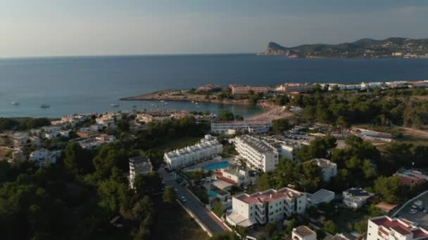 Establisher tiro de praia resort lateral com piscina e carros estacionados no estacionamento e pessoas relaxando na praia cercada por mar e montanhas em Ibiza, na Espanha — Vídeo de Stock