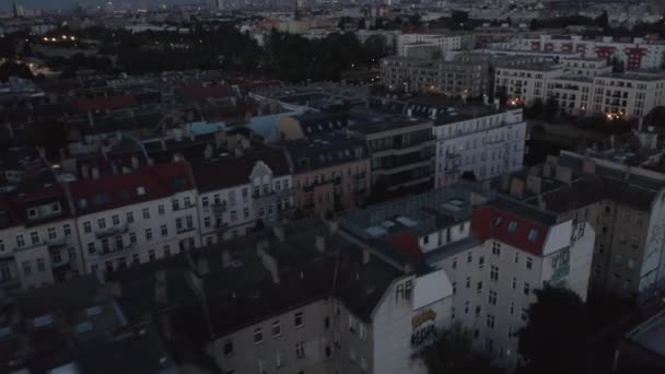 Nízký let nad multistorejskými obytnými budovami. Odhaluje městskou krajinu a míří k pěší křižovatce osvětlené oranžovým pouličním světlem. Město před východem slunce. Berlín, Německo — Stock video
