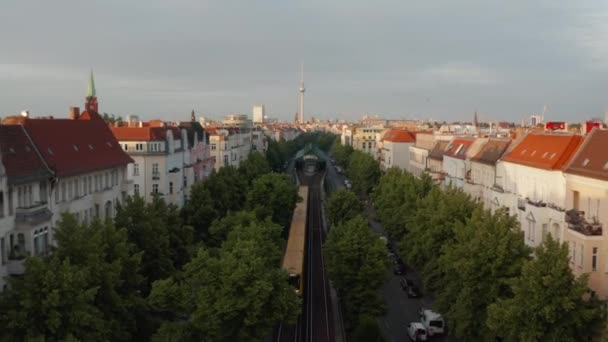 Baklänges spårning skanna tåg kör på bred gata med träd. Omgivande byggnader upplysta av ljus morgonsol. Fernsehturm TV-torn vid horisonten. Berlin, Tyskland — Stockvideo