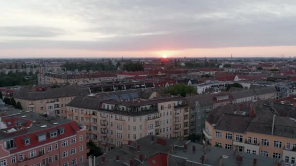 Backwards reveal of houses in urban neighbourhood. Fly above streets and buildings in city. View against rising sun. Berlin, Germany — Stock Video
