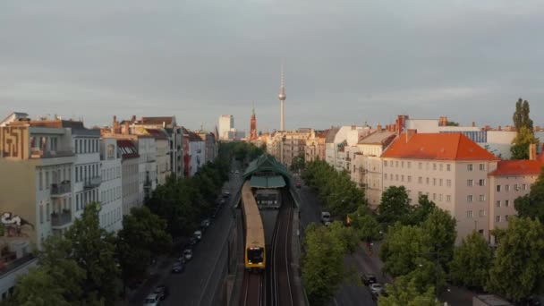 Şehirdeki geniş caddenin yukarısındaki tren istasyonundan ayrılan Sbahn trenini geriye doğru takip ediyoruz. Şehir merkezinin sabah manzarası. Arkadaki Fernsehturm TV kulesi. Berlin, Almanya — Stok video